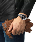 Hand wearing a silver watch with a brown leather wallet and glove, against a white background